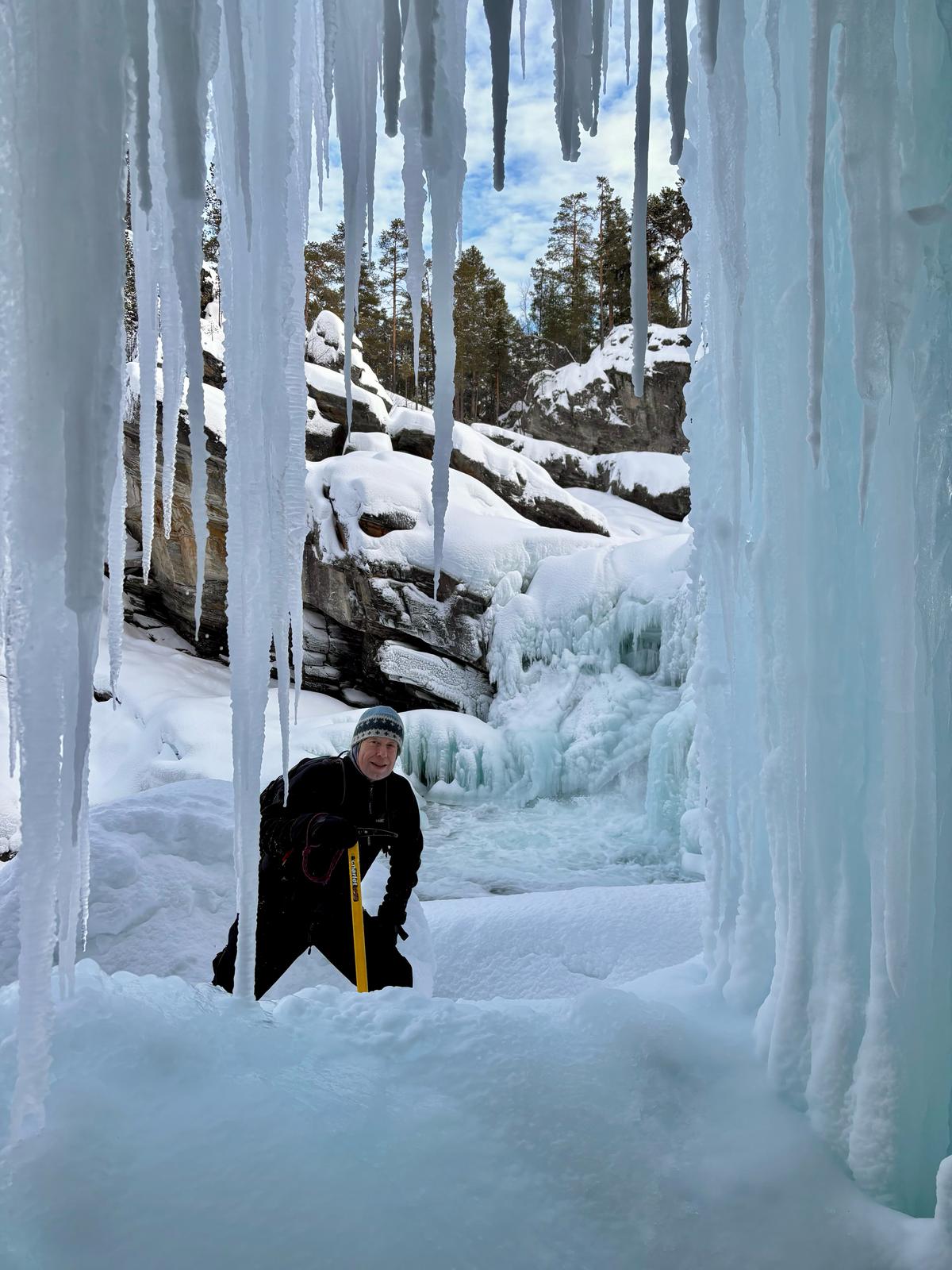 Guide med isøks foran en frossen foss i vinterlandskap