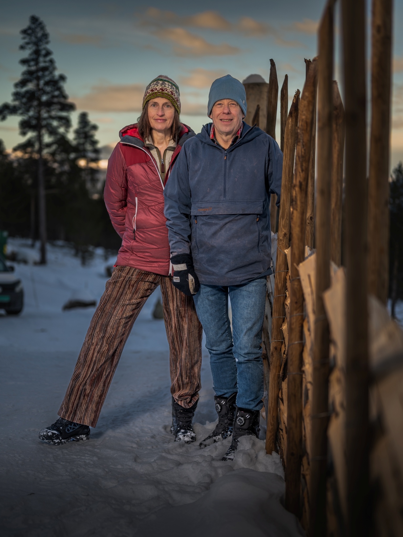 Mann und Frau in Winterkleidung bei Holzzaun vor Abendhimmel